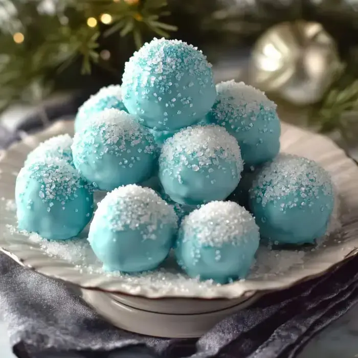 Un plato con bolitas de postre azules cubiertas en azúcar, similar a una escena nevada, rodeado de hojas festivas decorativas.