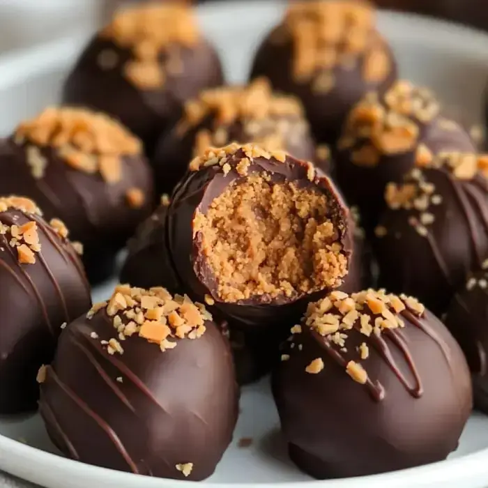 Un plano cercano de bolitas de postre cubiertas de chocolate, algunas con nueces por encima, y una mostrando el relleno cremoso con una mordida.