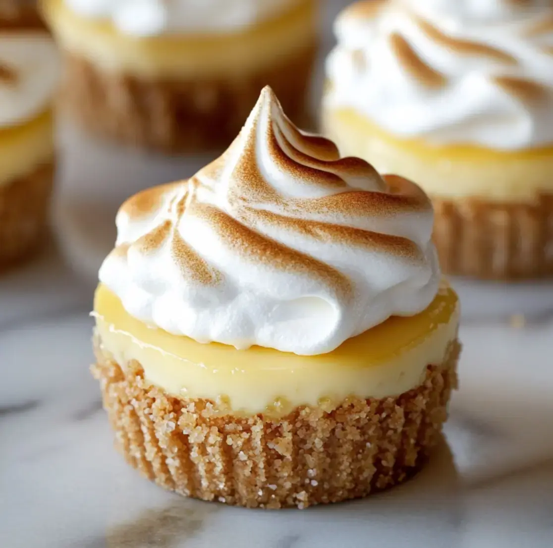 Primer plano de un cheesecake mini de limón con merengue doradito encima y base de galleta crujiente.