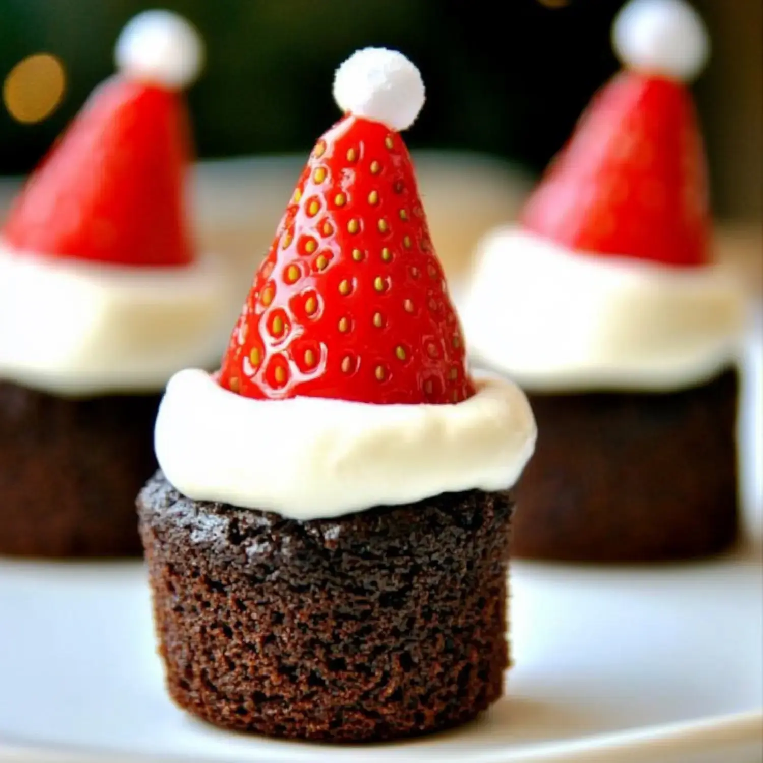 Un primer plano de magdalenas de chocolate cubiertas con crema blanca y una fresa en forma de gorro navideño.