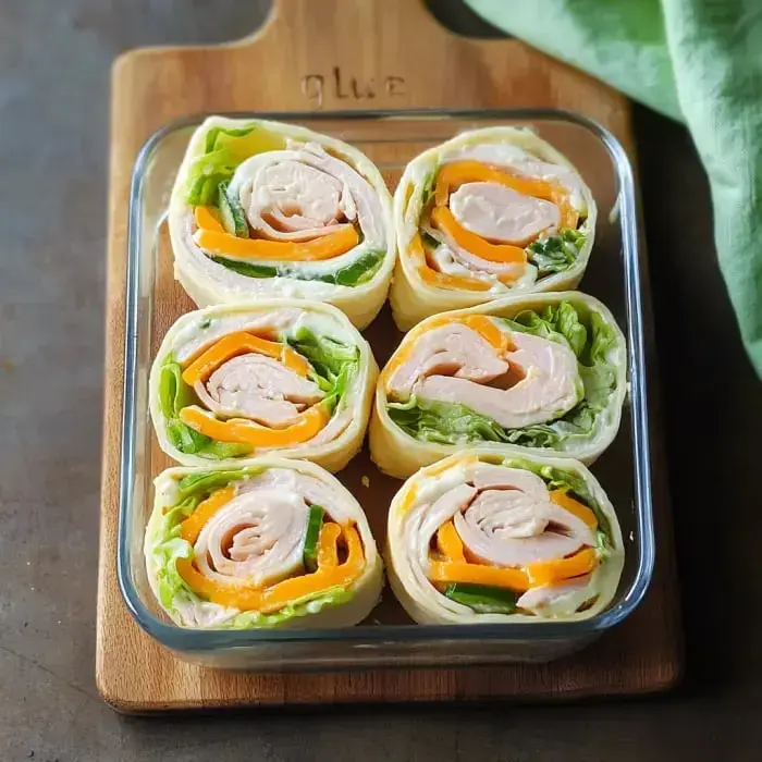 Un plato de cristal contiene seis rollitos hechos con tortitas, pavo, lechuga y pimientos coloridos ordenados pulcramente.