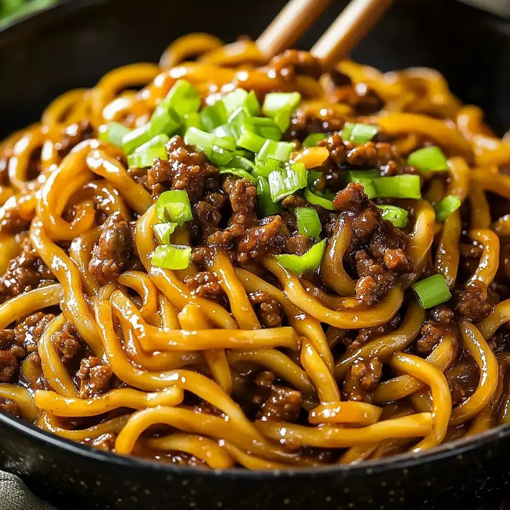 Un primer plano de un bol de fideos con carne picada y cebolletas picadas por encima.