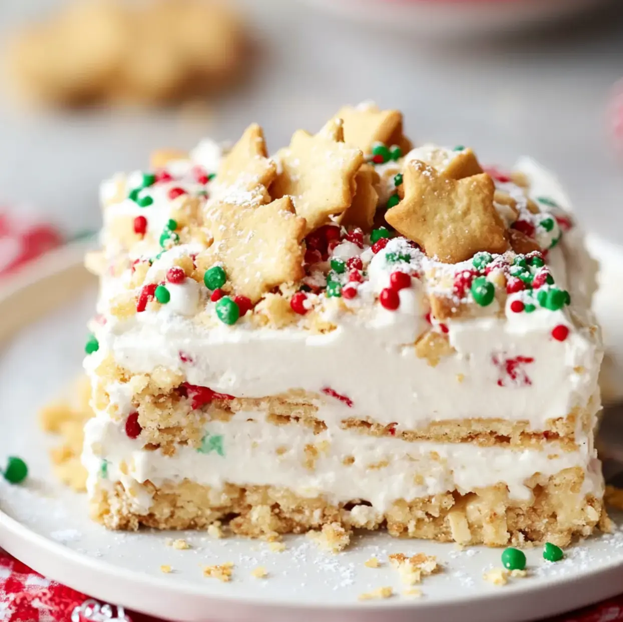 Una porción de postre en capas cubierto con nata montada, fideos de colores y galletas en forma de estrella en un plato blanco.